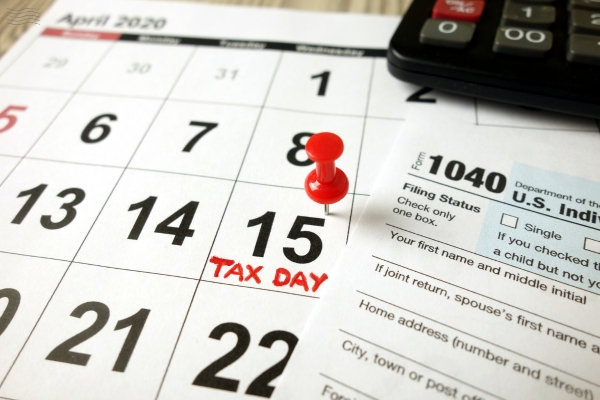 Form 1040 on top of a calendar with a red push pin on April 15 which is Tax Day in the United States.